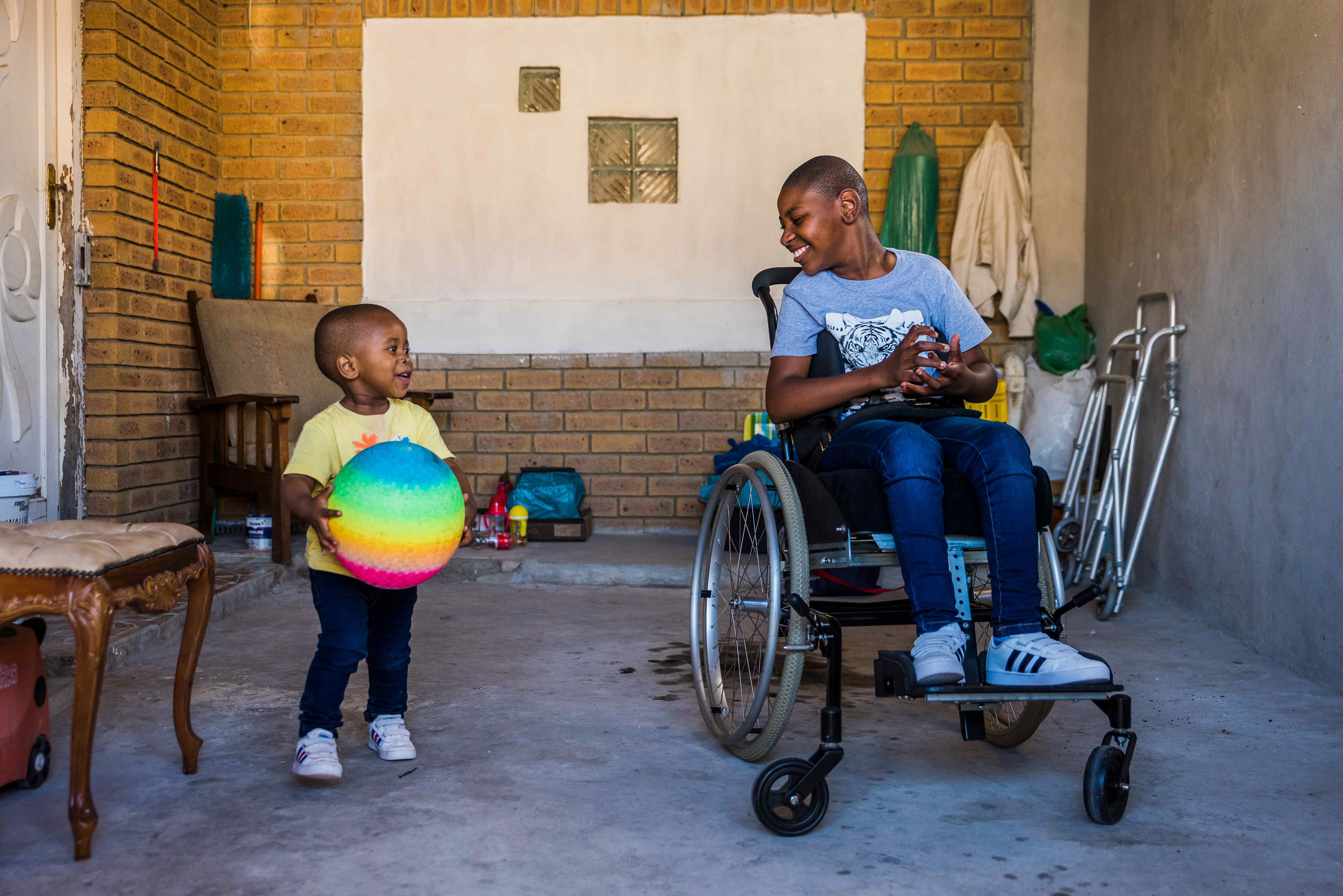 Image of two children playing with a ball, both are smiling and both are using wheelchairs Cover Image