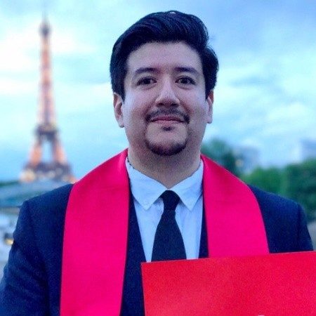 Felipe smiling while holding a diploma in front of the Eiffel Tower