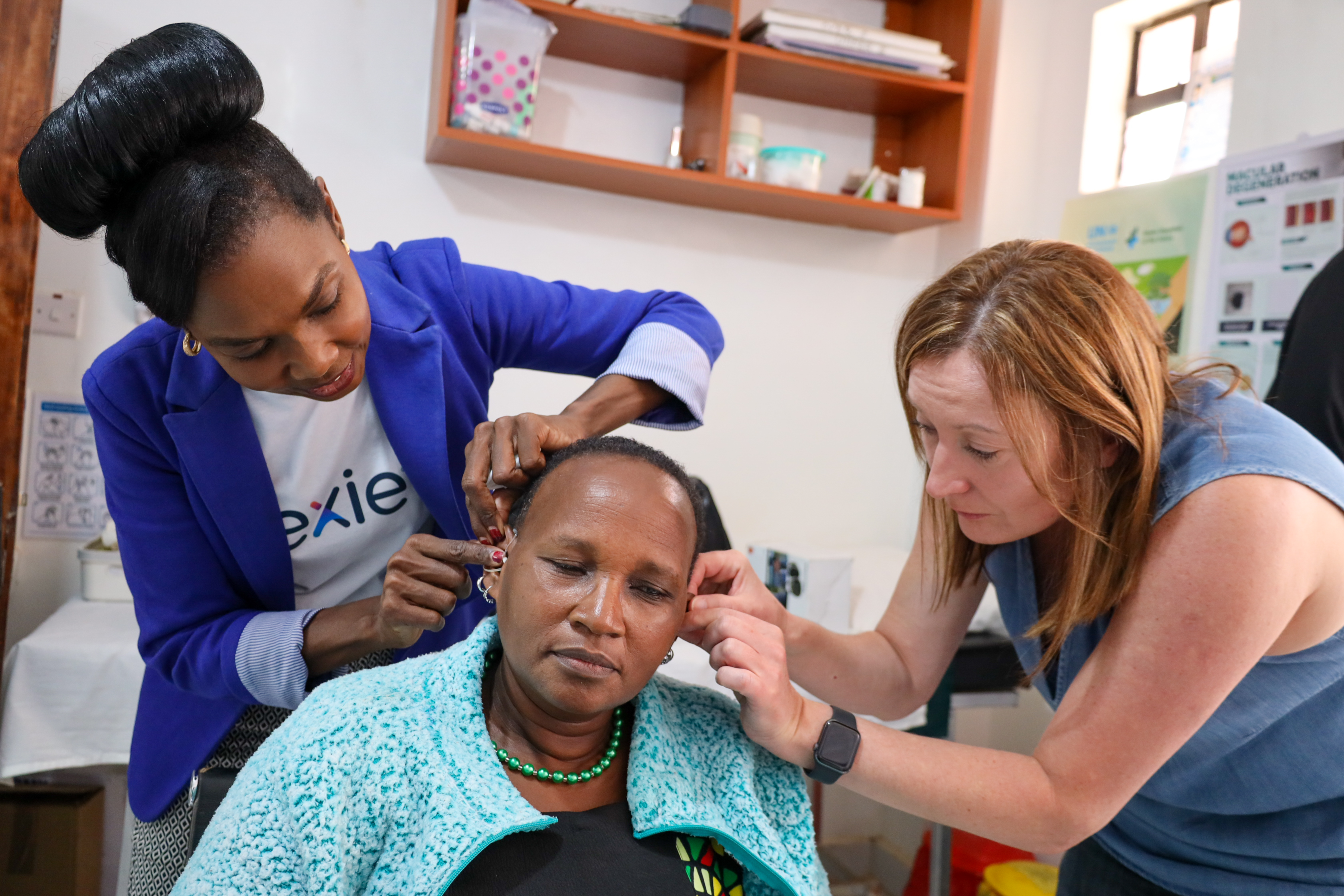 A person having a hearing aid fitted by two other people