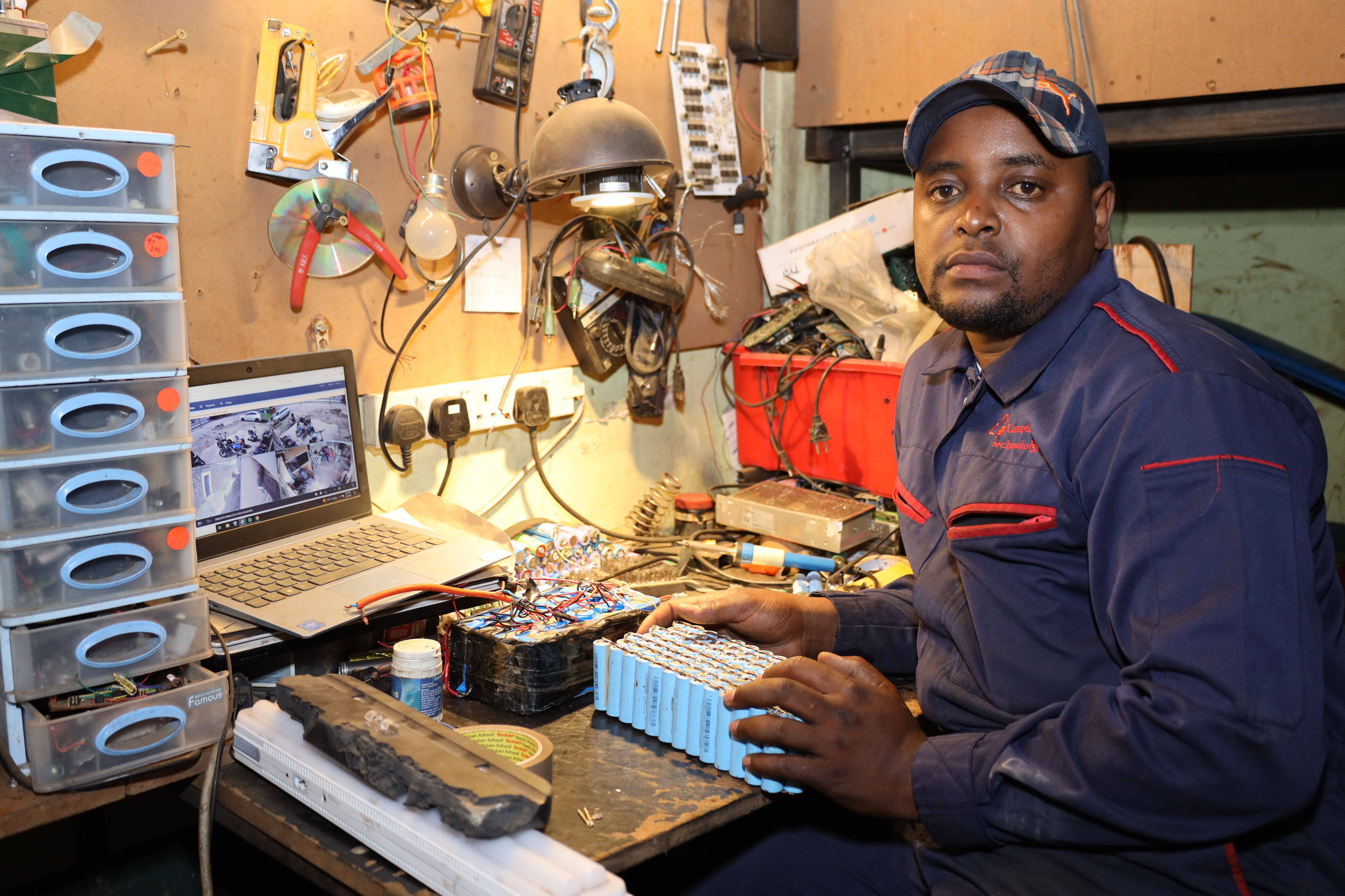 Lincon Wamae seated in his workshop where he works on his electric batteries Cover Image