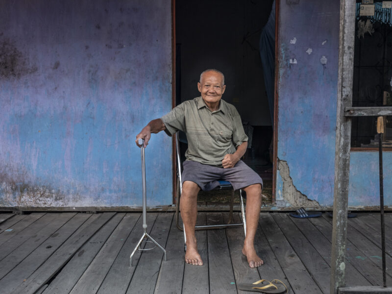 Image of man sitting with walking stick outside his house Cover Image