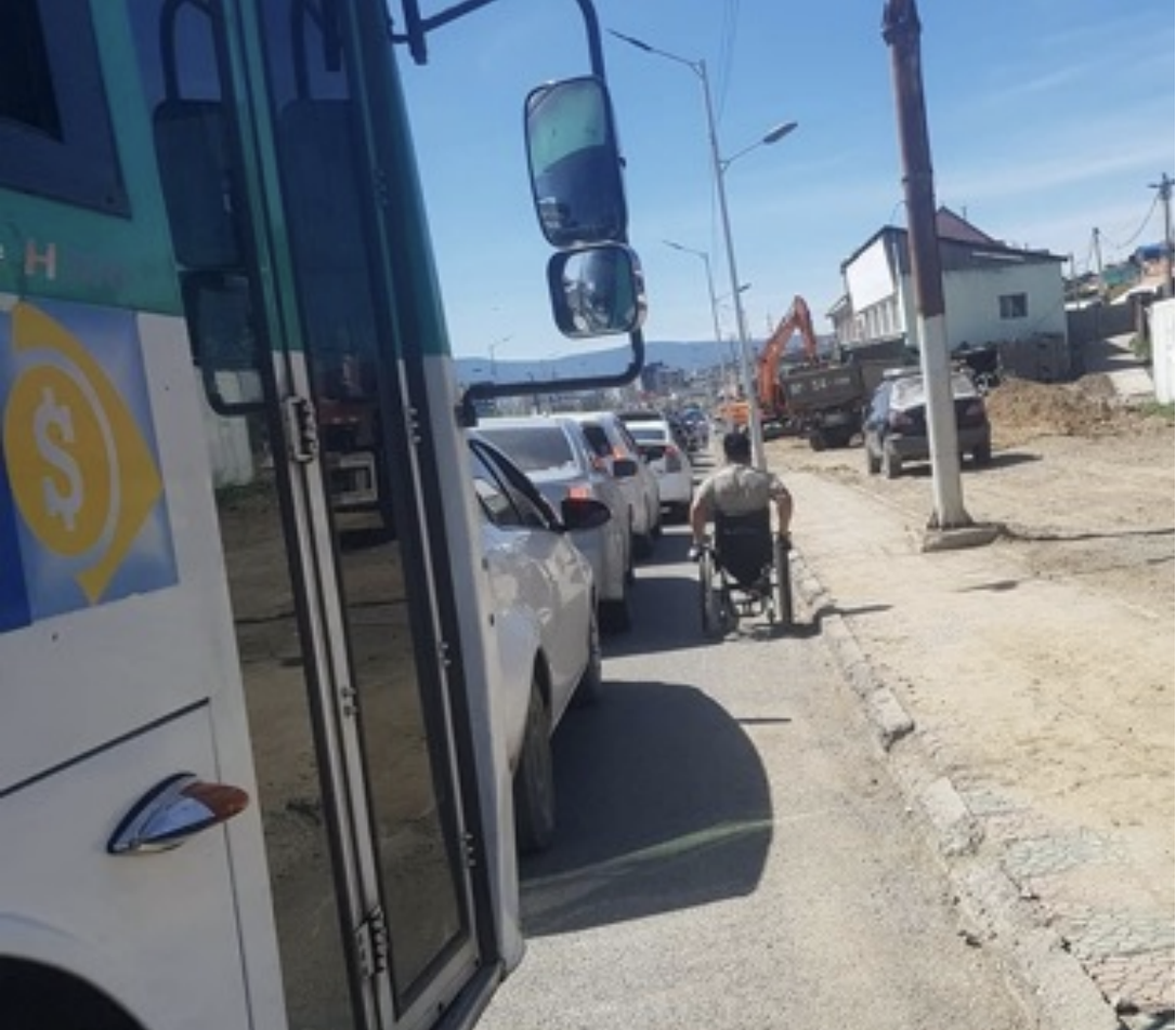 photo shows a person using their wheelchair on a busy road due to inaccessible pavement Cover Image