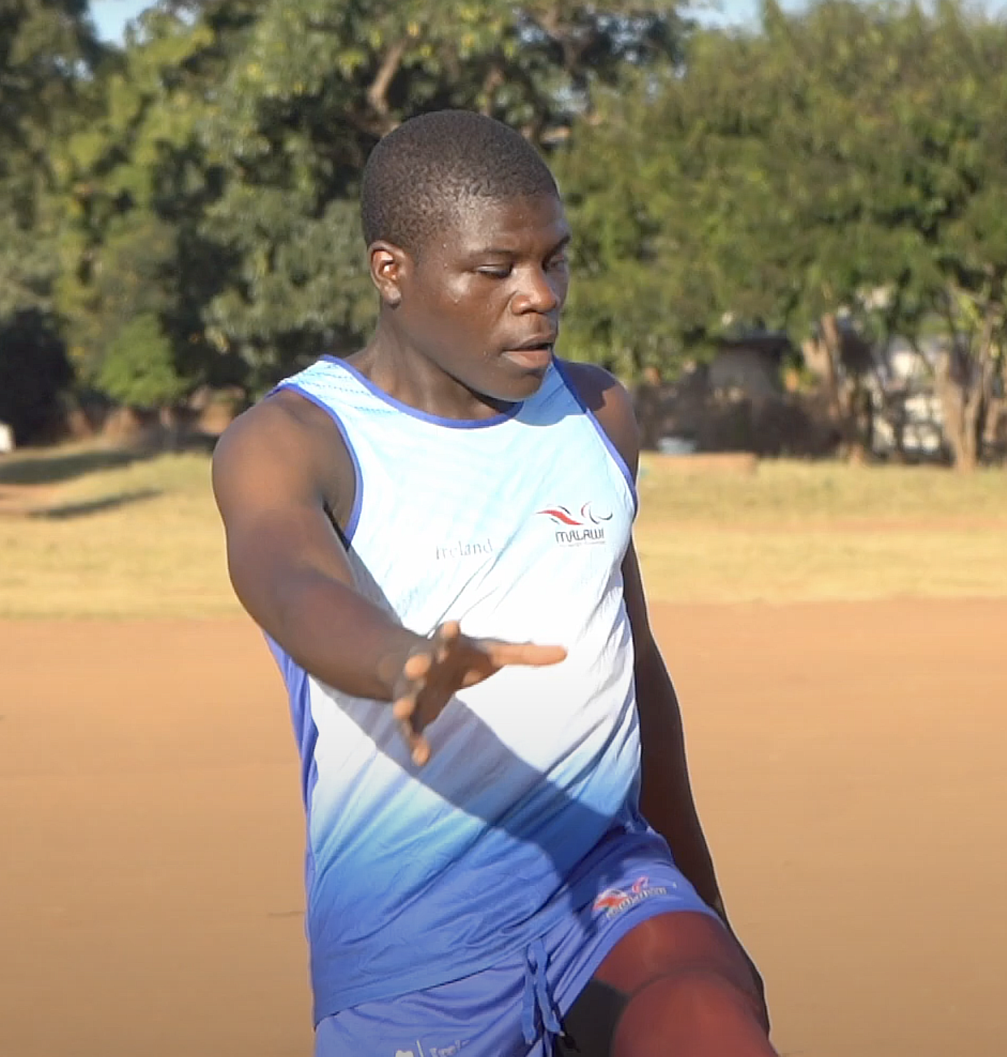 A male athlete wearing a blue and white singlet and blue shorts is in motion, with his left arm extended forward. Cover Image