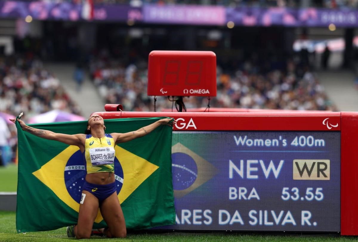 A Brazilian female athlete kneeling next to a screen with her world record