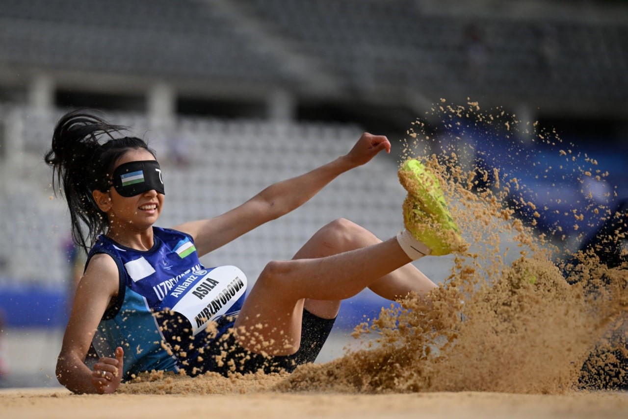 a woman with a blindfold landing after her long jump attempt. 