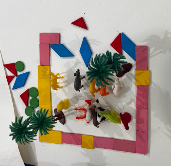 An outline made with wooden blocks illustrating pavement with toy animals and trees alongside depicting the flora and fauna that co-exist in urban and rural settings