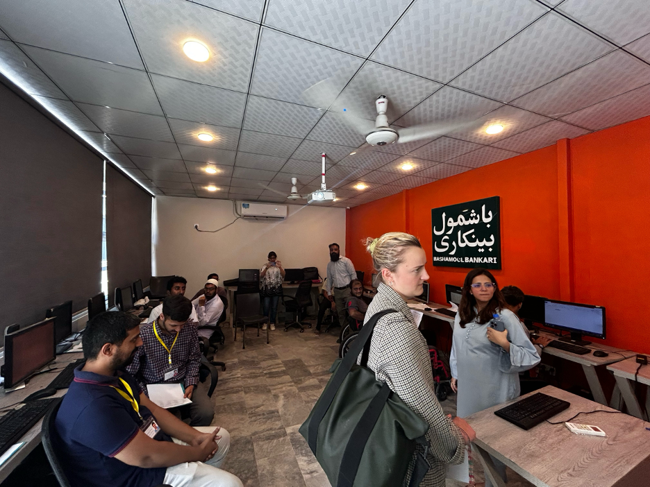 Pollyanna at NOWPDP Financial Inclusion teaching room. There is a frame on the wall titled "Bashamool Bankari" written in Urdi which means Inclusive Banking in English