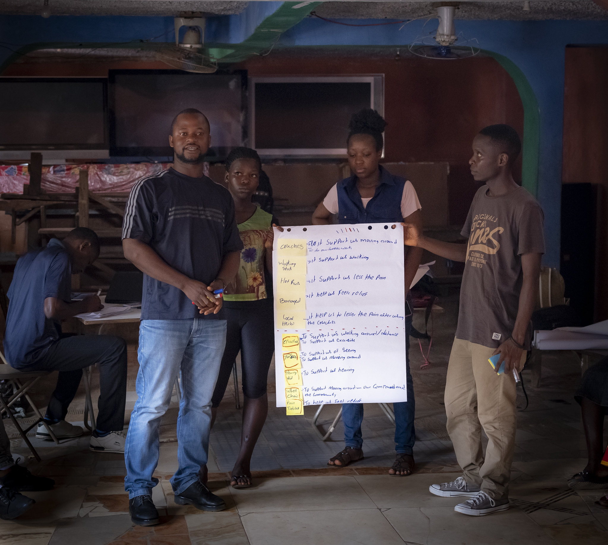 A group of participants standing next to a chart with sticky notes and handwriting describing uses of various Assisive Technologies