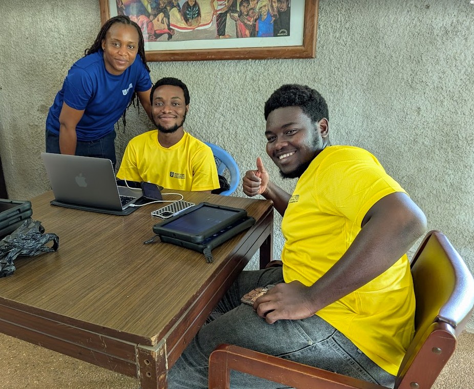 Three people sitting together and smiling at the camera, with devices during training 