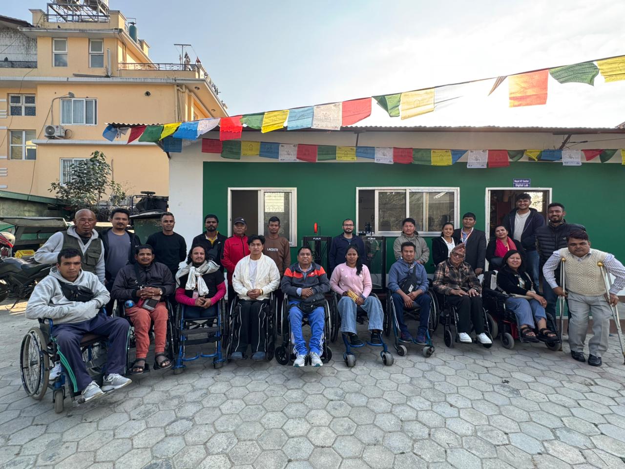 A large group of participants, including several using wheelchairs, pose for a group photo in front of a projector screen in a training room.