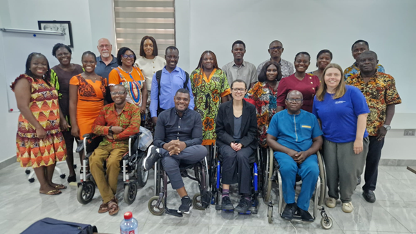 This photo is of around 20 people posing for a group photo at the end of the knowledge-sharing workshop. There are 4 wheelchair users in the front row. Everyone is smiling.