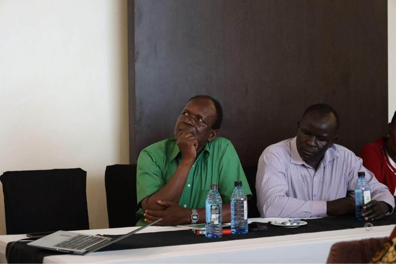 Two people sat at a meeting room table listening to the facilitator.