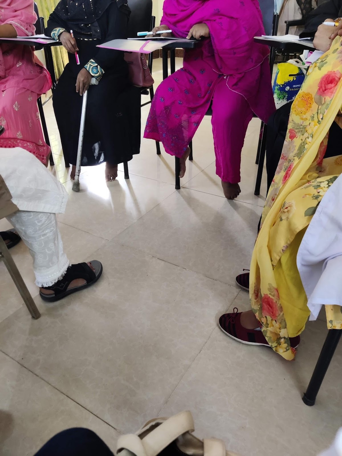 A group of women sitting in chairs. The Image only shows their body and legs, not their faces. There is a walking stick in view from one of the participants and they are sitting in a circle. 

Description automatically generated