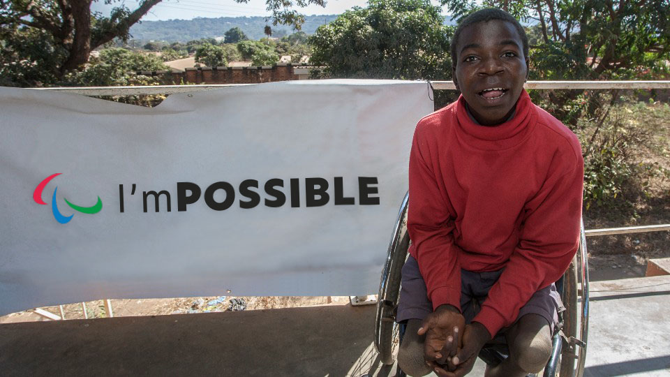 A wheelchair user sits in front of a banner that says "I'm possible"