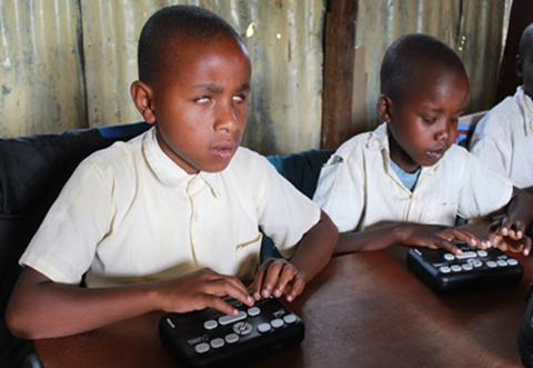 Two children sit side-by-side in a classroom using an orbit device with their fingers