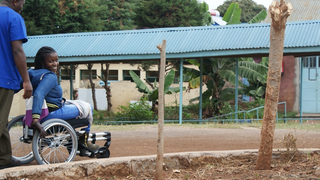 A woman is using a self-propelling wheelchair to push herself along a track. She is smiling back towards the camera