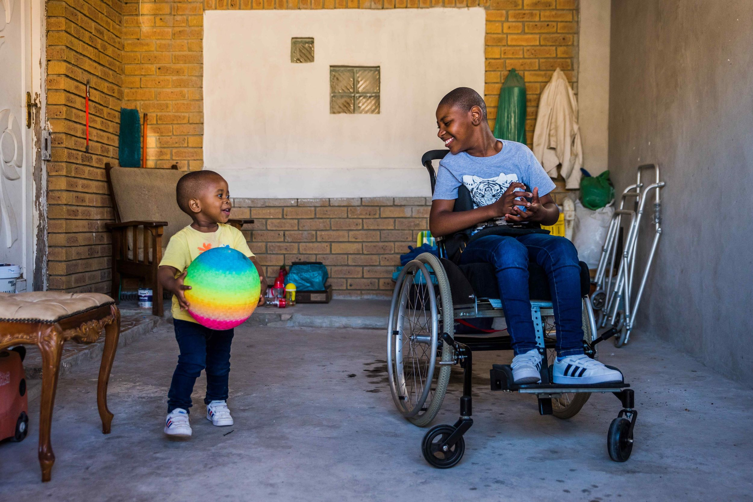 Image of two children playing with a ball - both are smiling and both are wheelchair users. Credit CHAI