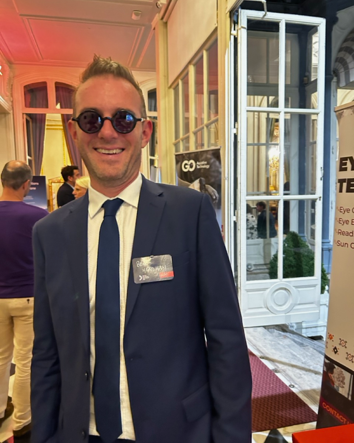 Ben Hardman smiling at the camera at The British Embassy in France. He is wearing sunglasses and a suit. Cover Image